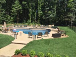 Residential landscaping project featuring a landscaped pool area with lounge chairs, surrounded by lush greenery and well-maintained grass, showcasing McLeod Landscaping's design and construction services.