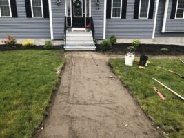 Residential landscaping project featuring a newly constructed walkway leading to a home, with freshly laid gravel, tools, and landscaping elements visible.