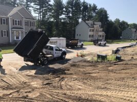 Construction site with McLeod Landscaping truck unloading materials, residential homes in background, showcasing hardscaping and landscaping work in progress.