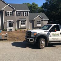 Residential landscaping project by McLeod Landscaping featuring a gray house, freshly prepared garden beds, and a branded work truck in the foreground.