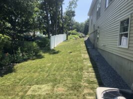 Residential landscaping project featuring a well-maintained grassy slope alongside a house, bordered by a white fence and surrounded by greenery, showcasing McLeod Landscaping's expertise in residential services.