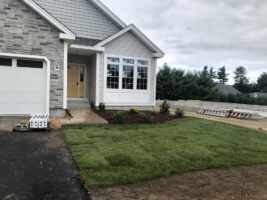 Residential landscaping project by McLeod Landscaping featuring freshly installed sod, flower beds, and a stone façade home entrance.