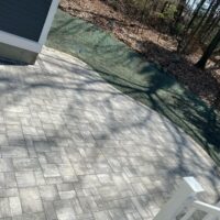 Paved patio installation showcasing a stone surface, surrounded by natural landscaping and shadows from nearby trees, reflecting McLeod Landscaping's residential hardscaping services.