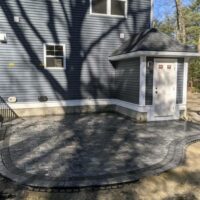 Residential hardscape project featuring a circular stone patio adjacent to a house, showcasing professional masonry work by McLeod Landscaping.