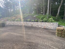 Residential landscaping project featuring a stone retaining wall with greenery, surrounded by a gravel area and hay bales, showcasing McLeod Landscaping's hardscaping services.