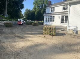 Residential landscaping project featuring freshly laid sod rolls and a compact loader on a prepared yard near a white house, showcasing McLeod Landscaping's installation services.