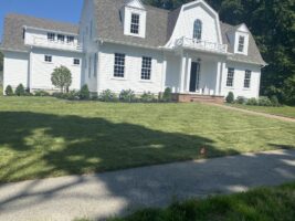 Residential landscaping project by McLeod Landscaping featuring a well-maintained white house, manicured lawn, and clear walkways.