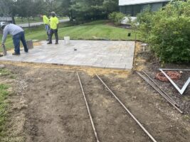 Workers installing a stone patio in a residential landscaping project, showcasing McLeod Landscaping's masonry services.