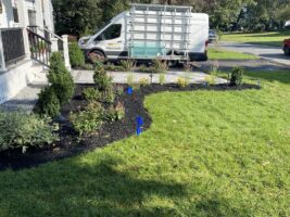Residential landscaping project by McLeod Landscaping featuring newly planted shrubs and flowers, freshly mulched flower beds, and a service vehicle in the background.